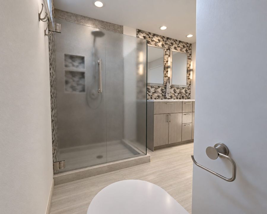 3D rendering of the same bathroom from the doorway: a frosted glass shower with niches, the gray wood double vanity, and the pebble mosaic wall with crystal sconces