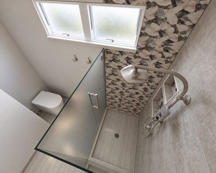 Overhead 3D rendering of the same bathroom: shower with a frosted glass door, brushed nickel rain shower and hand shower, the pebble mosaic wall, and a wall-hung toilet