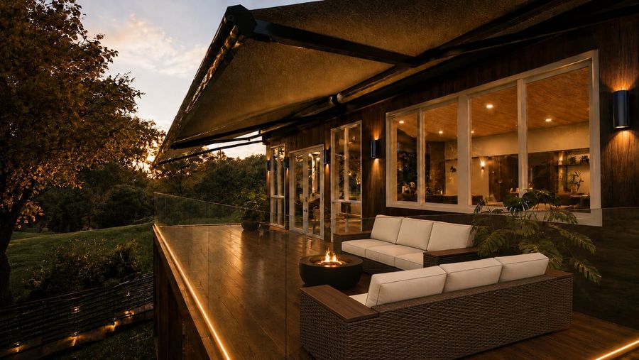 3D rendering at dusk of the same home's upper deck: wicker sectional seating with cream cushions, a fire bowl, a glass railing with a warm LED edge, and a retractable awning